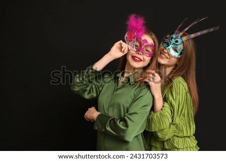 Happy young women in carnival masks on black background