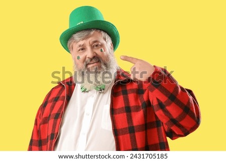 Mature man in hat pointing at drawn Irish flag on yellow background. St. Patrick's Day celebration