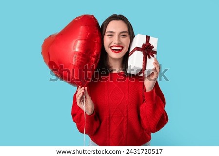 Beautiful young happy woman with gift box and heart-shaped balloon on blue background. Valentine's Day celebration