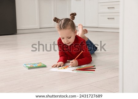 Cute little girl coloring drawing on warm floor in kitchen. Heating system