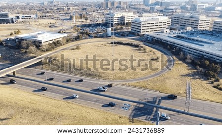 Large college campus near I-235 Highway loop with office buildings and rooftop parking garage, busy downtown Centennial Expressway, high rises urban apartment complex, skyscraper background. Areial