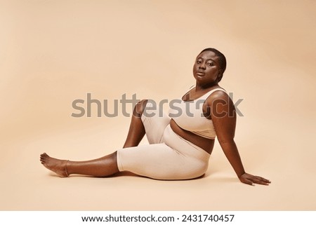 plus size african american young woman in beige underwear posing against matching backdrop