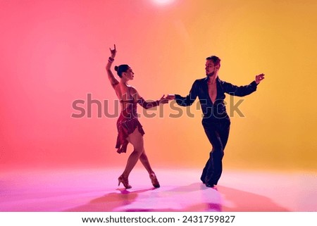 Male and female dancers performing a Latin dance in stylish clothes against gradient pink yellow background in neon light. Concept of dance class, hobby, art, dance school, talent