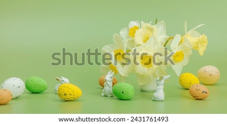 Blooming daffodils with Easter eggs and rabbits on light green background. Happy holiday concept, greeting card, traditional festive composition, banner format