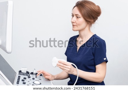Female doctor woman in uniform sitting in office in a hospital with ultrasound diagnostic machine equipment and ready to examine patients and do ultrasound of heart, thyroid gland or abdominal cavity Royalty-Free Stock Photo #2431768151