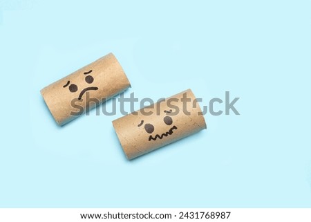 Cardboard center of a toilet paper rolls without paper with and sad faces drawn on a blue background with copy space Royalty-Free Stock Photo #2431768987