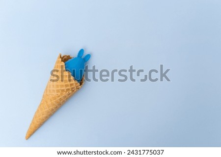 A waffle ice cream cone with a hidden blue Easter egg with ears like a bunny on a blue background, concept, copy space, flat lay. Minimalist Easter greeting card. Easter Hunter