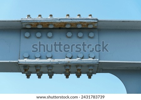 Parts of a modern metal bridge in close-up against a blue sky background. Metal structures connected by large bolts and nuts to a reinforced concrete base. Railway or automobile bridge.