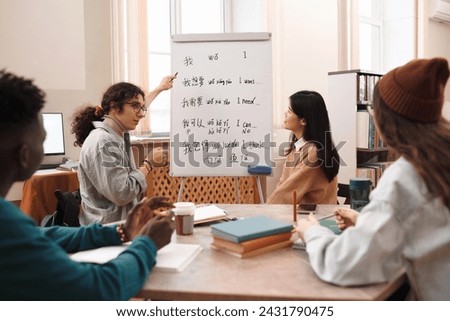 Side view portrait of male student answering questions during Chinese language class and pointing at whiteboard with hieroglyphs Royalty-Free Stock Photo #2431790475