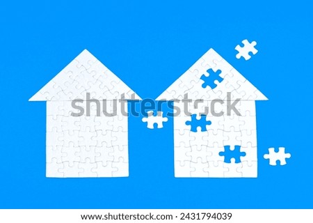Complete and incomplete white house shapes made up from jigsaw puzzle elements isolated on blue. Some final elements are set aside. Royalty-Free Stock Photo #2431794039