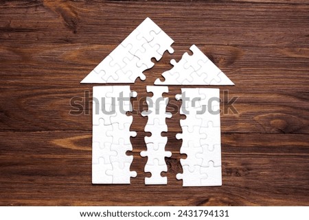 Disintegrated jigsaw puzzle in the shape of a roofed house isolated on a dark wooden backdrop. Construction and development concept.