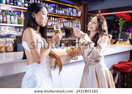 Two women engaging in a friendly conversation with drinks at a chic bar, surrounded by a warm and inviting atmosphere.