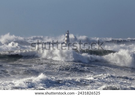 Rough sea with big stormy waves. Northern portuguese coast. Entry of Povoa do Varzim and Vila do Conde harbor. Focus on the lighthouse.