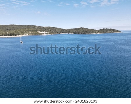 A drone picture of a single sailing yacht moored in deep blue water with lush green mountains in the background