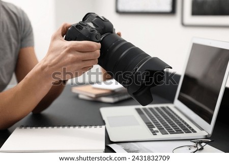 Professional photographer with digital camera at table indoors, closeup