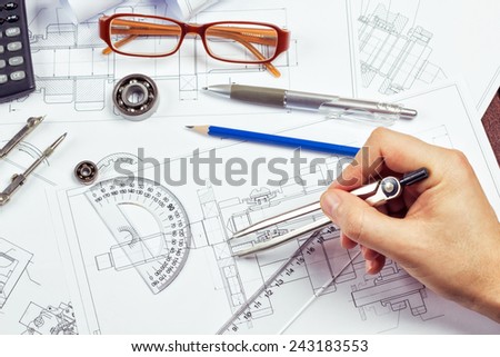 Drawings, pencil, pen, protractor, compass bearings, calculator on the table. Man's hand with a compass. The process of drawing. Department of engineering design.