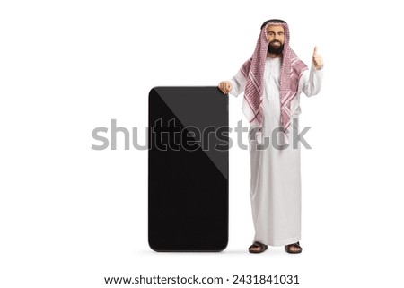 Saudi arab man in ethnic clothes leaning on a big mobile phone and gesturing thumbs up isolated on white background