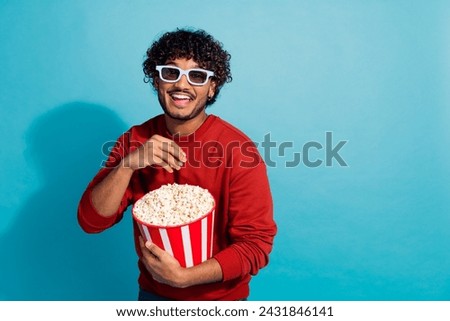 Photo of young mexican guy wavy hair dressed red sweatshirt eat popcorn in 3d glasses weekend resting isolated on blue color background