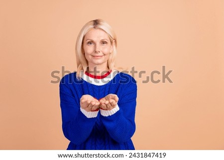 Photo of thankful optimistic woman dressed knitwear sweater palms presenting product empty space isolated on beige color background