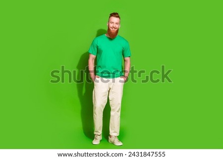 Full size photo of confident cool guy with long red beard wear stylish t-shirt keep arms in pockets isolated on green color background