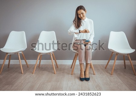Portrait of confident serious young Asian female sitting on chair in waiting room with electronic tablet, setting her mind up before job interview or meeting with potential business partners