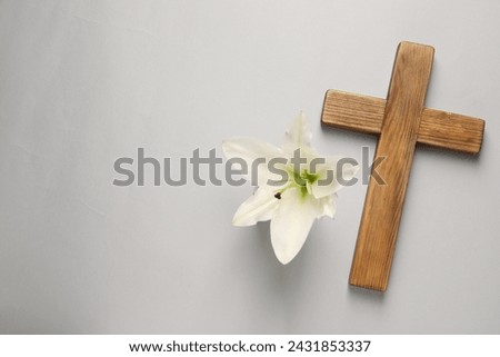 Wooden cross and lily flower on grey background, top view with space for text. Easter attributes