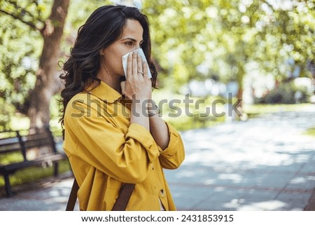 Portrait of unhealthy cute  female in yellow top with napkin blowing nose, looks to the source of the allergy, place for advertising. Rhinitis, cold, allergy concept. Pollen allergy symptoms Royalty-Free Stock Photo #2431853915