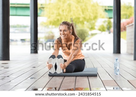 Woman stretching at park while listening to music. Young woman working out at sunset. Healthy sport girl doing stretching exercise early in the morning at park.