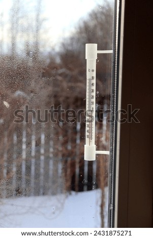A plastic mercury or alcohol thermometer outside the window of a village house on a frosty day. View from the window into the courtyard, vertical photo Royalty-Free Stock Photo #2431875271