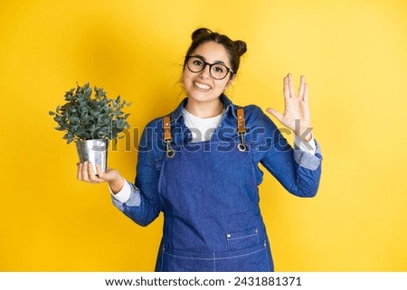 Young caucasian gardener woman holding a plant isolated on yellow background doing star trek freak symbol