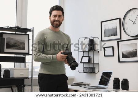 Professional photographer holding digital camera near table with laptop in office