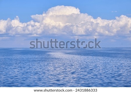 A tranquil seascape with gentle ripples on the water and billowy white clouds in the sky, their reflections dancing on the serene surface, creating a harmonious interplay of light and nature Royalty-Free Stock Photo #2431886333