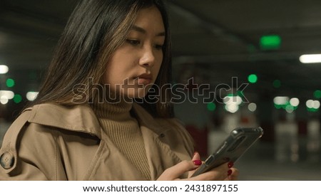 Serious Asian woman chinese korean japanese woman girl ethnic lady client customer driver in underground car parking chatting mobile phone application typing message browsing internet cellphone chat Royalty-Free Stock Photo #2431897155