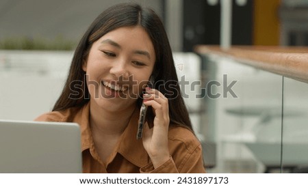 Smiling Asian woman businesswoman working online with laptop in office chinese japanese girl student freelancer talk mobile phone laughing excited female answer smartphone call carefree conversation Royalty-Free Stock Photo #2431897173