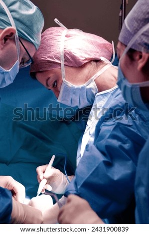 Surgeon and assistant performing cosmetic surgery in hospital operating room. Surgeon in mask wearing loupes during medical procadure. Breast augmentation, enlargement, enhancement, breast cancer Royalty-Free Stock Photo #2431900839