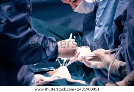 Surgeon and assistant performing cosmetic surgery in hospital operating room. Surgeon in mask wearing loupes during medical procadure. Breast augmentation, enlargement, enhancement, breast cancer Royalty-Free Stock Photo #2431900851