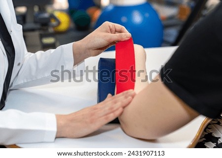 Physical therapist placing kinesio tape on patient's elbow. Therapy with kinesio tex tape. Therapeutic treatment of elbow with kinesio tape. kinesio treatment after sports muscle injury.  Royalty-Free Stock Photo #2431907113