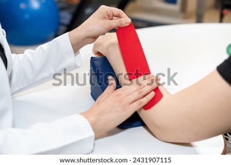 Physical therapist placing kinesio tape on patient's elbow. Therapy with kinesio tex tape. Therapeutic treatment of elbow with kinesio tape. kinesio treatment after sports muscle injury.  Royalty-Free Stock Photo #2431907115