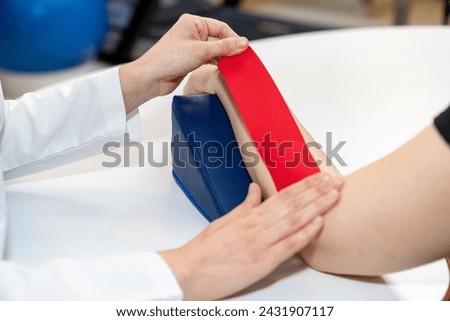 Physical therapist placing kinesio tape on patient's elbow. Therapy with kinesio tex tape. Therapeutic treatment of elbow with kinesio tape. kinesio treatment after sports muscle injury.  Royalty-Free Stock Photo #2431907117