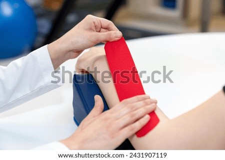 Physical therapist placing kinesio tape on patient's elbow. Therapy with kinesio tex tape. Therapeutic treatment of elbow with kinesio tape. kinesio treatment after sports muscle injury.  Royalty-Free Stock Photo #2431907119