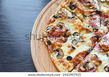Sliced pepperoni and mushroom pizza with black olives and melted cheese, served on a wooden pizza board on a dark table