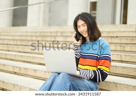Multitasking Oriental Student on Stairs: Laptop and Phone Use Reflect Modern Study Habits and Busy Academic Life Royalty-Free Stock Photo #2431911587