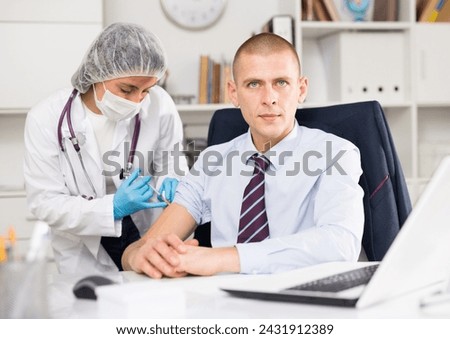 Medical nurse in safety gloves and protective mask making vaccine injection to a patient in health clinic Royalty-Free Stock Photo #2431912389