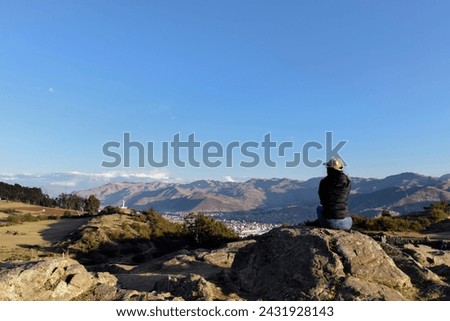 Successful traveler returns to the pictures Rear view image of a female traveler seat on rock Saqsaywaman Inca archaeological site. Cusco Peru