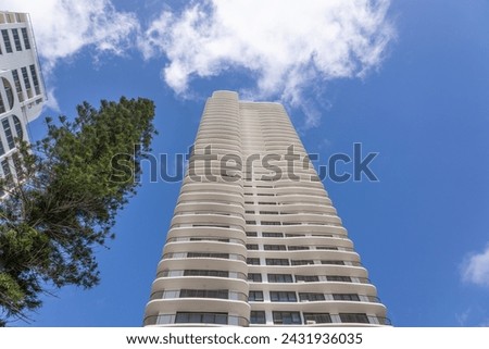 A pine tree versus modern apartment buildings in a upwards diminishing perspective view with blue sky and clouds on the Gold Coast in Queensland, Australia. Royalty-Free Stock Photo #2431936035