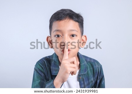Casual style little boy asking to be quiet with finger on lips on grey background. Keep secret and silent concept.