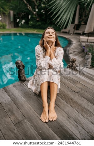 Beautiful caucasian lady in dressi sitting near swimming pool   at tropical summer resort, closed eyes, meditation Royalty-Free Stock Photo #2431944761
