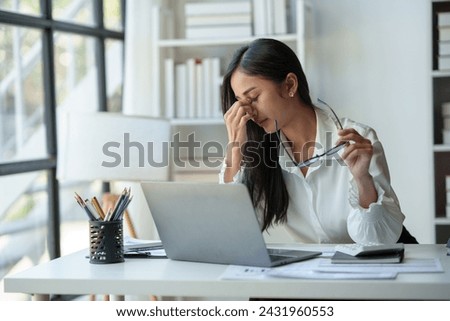 Asian businesswoman is tired, headache, sleepy and bored from sitting at a desk for a long time working on a laptop computer. Problematic financial paperwork Office syndrome concept.