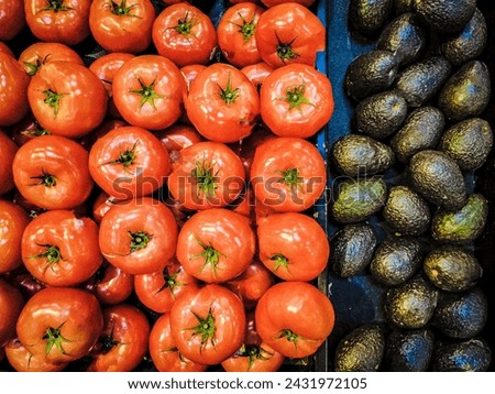 Tomatoes and avocados are stacked on a cart at a market.