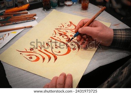 Writing in Arabic in Kufa script. Calligraphy. 
A person draws on paper using a pen. Includes items such as handwriting, office supplies, drawing, stationery, children's art, scissors, art and ink. 